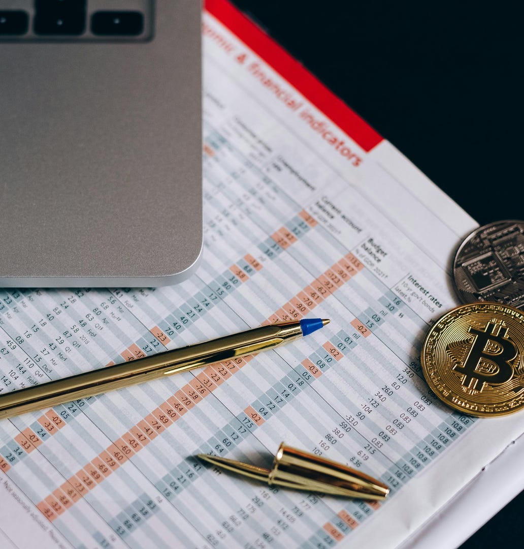Flat lay of Bitcoin coins on a financial report with a laptop and pen.